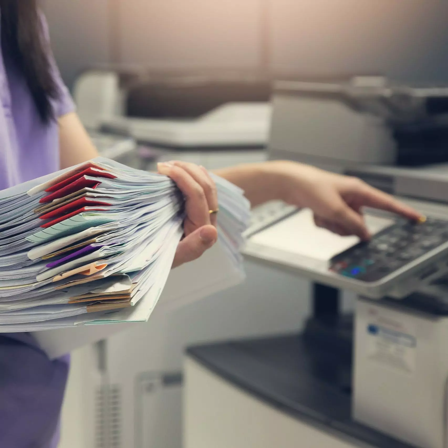 Bussinesswoman using copier machine to copy heap of paperwork in office.