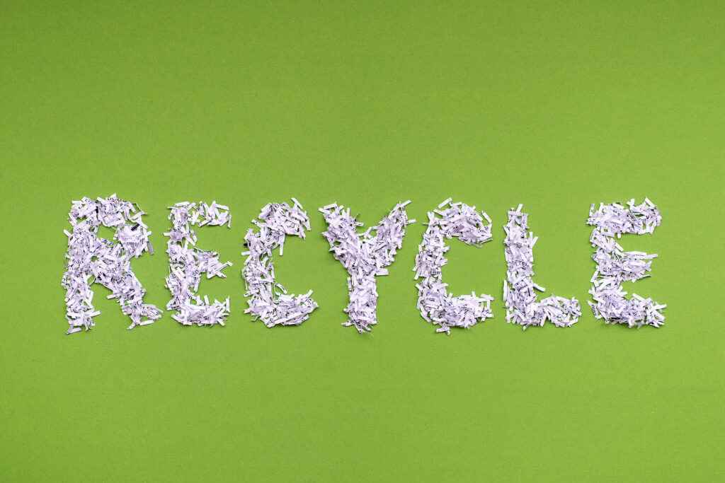 The word recycle is made from a heap of shredded white paper on green background